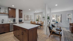 Een moderne keuken met houten kastjes, een centraal eiland, een eethoek met tafel en stoelen, en een zithoek met een bank en salontafel.