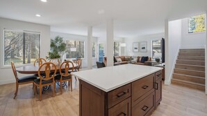 Een ruime woonruimte met een eettafel, stoelen, een groot schiereiland en een trap naar een hoger gelegen verdieping.