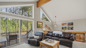 A spacious living room with a large window, a leather sofa, a wooden coffee table, and a staircase leading to a deck.