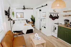 Quarto de hotel compacto com cama, um pequeno espaço para sentar, cozinha compacta e ventoinha no teto.