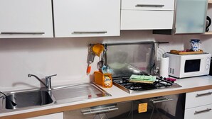Een keuken met witte kastjes, een roestvrijstalen spoelbak, een gasfornuis en een magnetron.