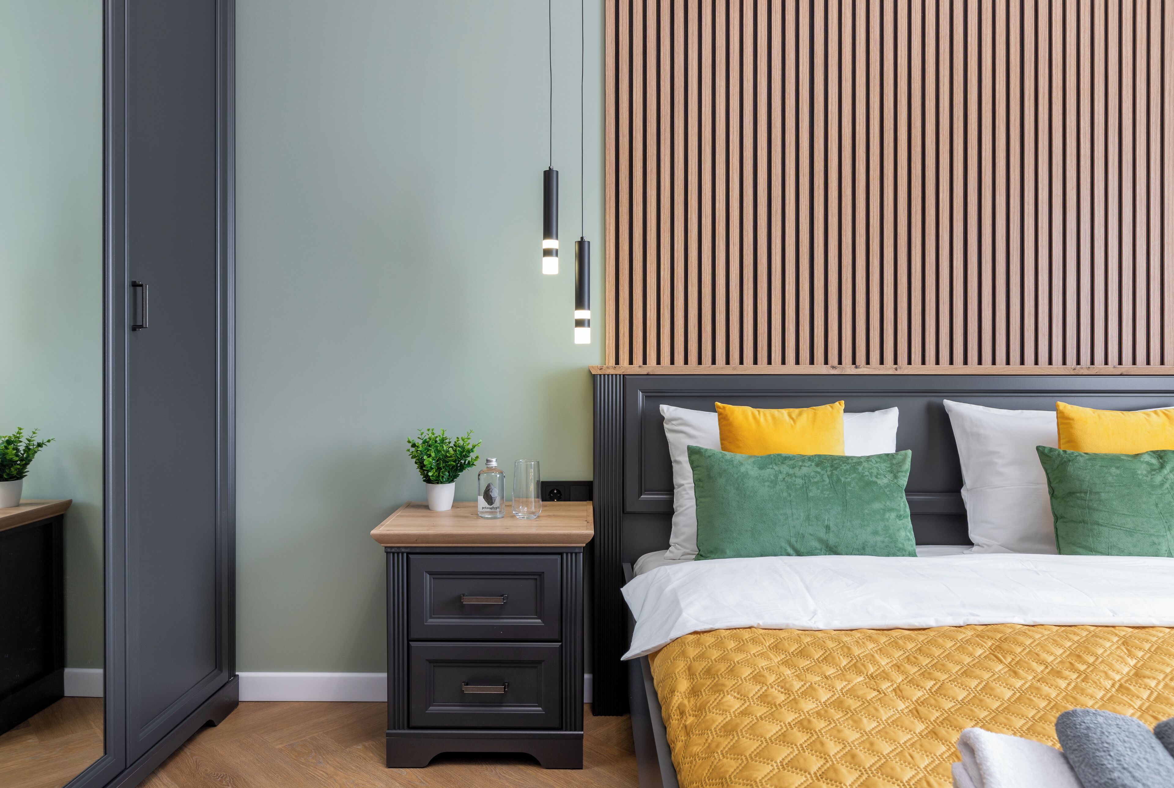 A bedroom with a bed, bedside tables, a nightstand, a wooden slat wall, and a hanging light fixture.