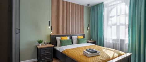 Un dormitorio moderno con cama, mesitas de noche, un velador, una estantería en la pared y una ventana con cortinas.