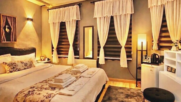 A hotel room with a large bed, two bedside tables, a desk, a chair, and a window with curtains. - Roza Mitra Butik Otel (İstanbul)