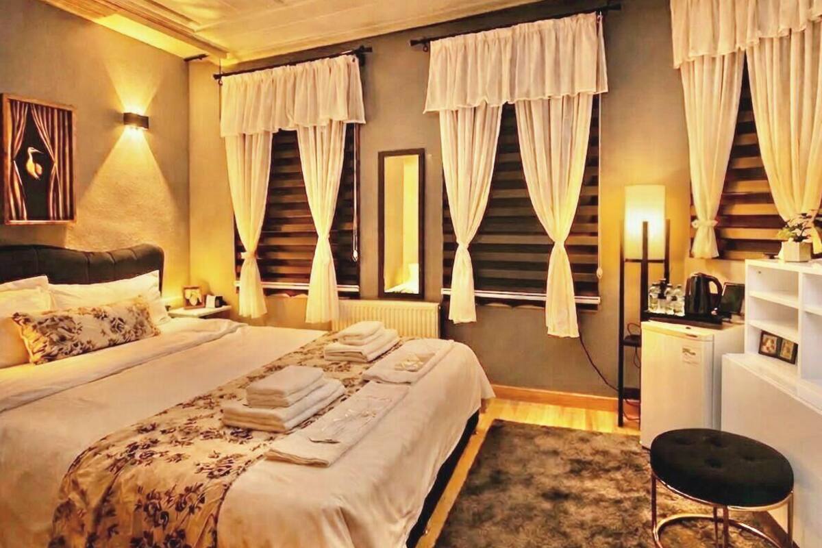 A hotel room with a large bed, two bedside tables, a desk, a chair, and a window with curtains.