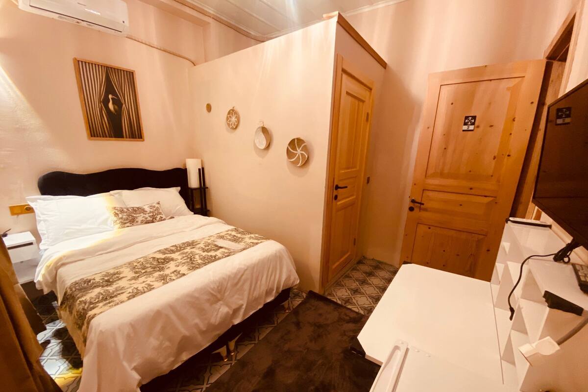 A hotel room with a bed, a desk, a chair, a wardrobe, and a door.