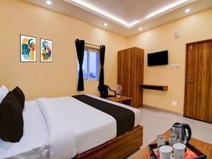 Habitación de hotel con cama, televisión, armario de madera, ventana con cortinas y obras de arte en la pared.