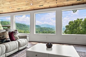 Ein Zimmer mit einer Couch, einem Couchtisch und großen Fenstern mit Blick auf die Berge.