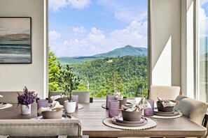 Ein Essbereich mit Blick auf ein bewaldetes Gebirge, einem Gemälde an der Wand und einer modernen Tischdekoration.