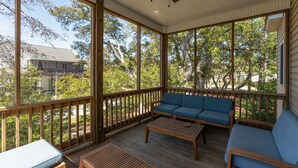 A covered porch with wooden railings, a blue sofa, and a wooden table. - Walk to Beach Arcade Games Family Friendly Oak Island (Oak Island)