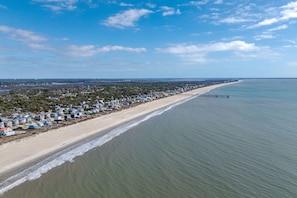 A coastal area with a long beach, a pier extending into the water, and a dense cluster of buildings along the shore. - Walk to Beach Arcade Games Family Friendly Oak Island (Oak Island)