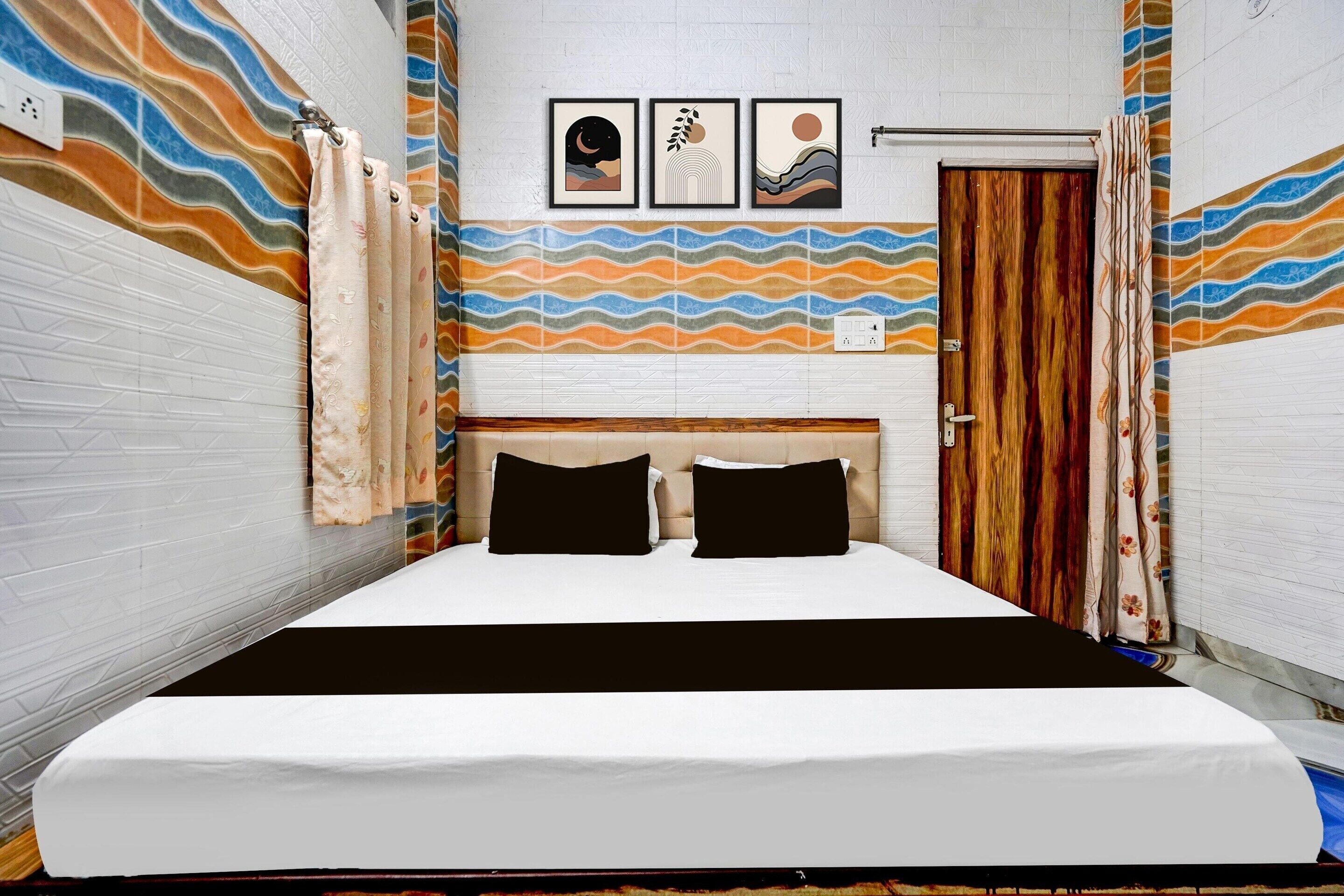 A hotel room with a bed, a wooden headboard, a wall with a wavy pattern, and three framed pictures above the bed.