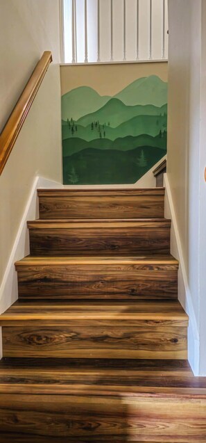 Eine hölzerne Treppe mit einem Wandgemälde von einer grünen Landschaft.