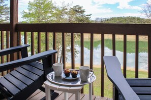 Eine Terrasse mit zwei Stühlen, einem kleinen Tisch mit einer Ablage, auf der zwei Muffins und zwei Tassen stehen, und Blick auf einen See.