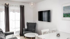 A modern living room with a sofa, a grey armchair, a round table, and a flat-screen TV mounted on the wall. - Comfortable House With a Terrace, Sauna, Jacuzzi (Rewal)