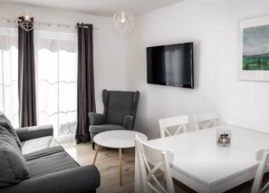 A modern living room with a sofa, a grey armchair, a round table, and a flat-screen TV mounted on the wall. - Comfortable House With a Terrace, Sauna, Jacuzzi (Rewal)