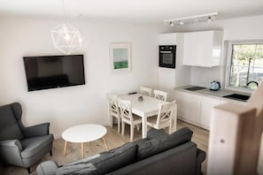 A modern, compact living space with a flat-screen TV, a dining area, a kitchenette, and a sofa. - Comfortable House With a Terrace, Sauna, Jacuzzi (Rewal)