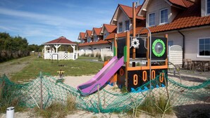 A playground with a slide and a climbing structure, surrounded by houses with red roofs and a fenced area. - Comfortable House With a Terrace, Sauna, Jacuzzi (Rewal)