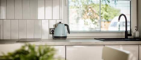 A modern kitchen with white cabinets, a kettle, and a window with blinds.