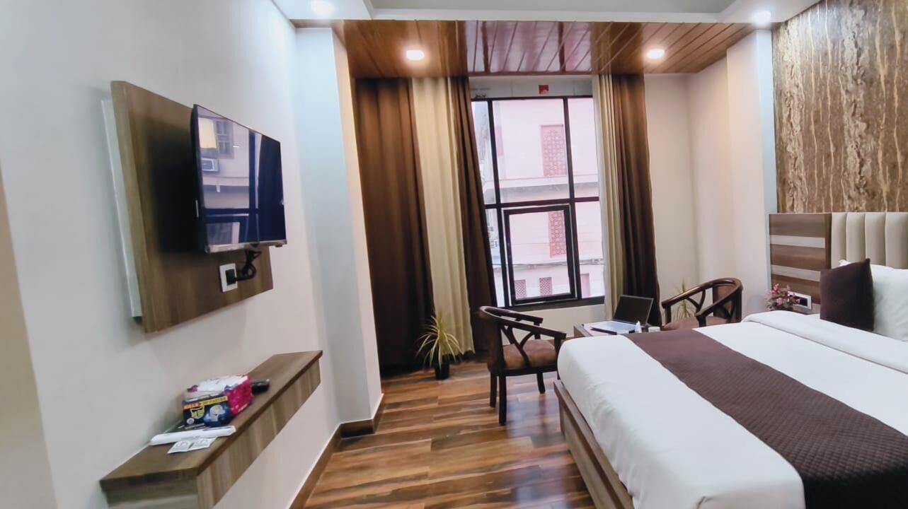 Une chambre d’hôtel avec un lit, un bureau, une chaise, une télévision et une fenêtre avec des rideaux.