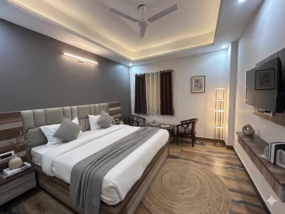 A modern hotel room with a large bed, bedside tables, a desk, a chair, a ceiling fan, and a TV mounted on the wall.