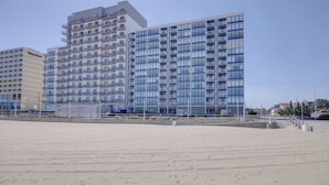 Et hotel ved stranden med flere etager, altaner og en sandstrand i forgrunden.