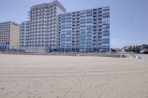 A beachfront hotel with multiple floors, balconies, and a sandy beach in the foreground. - Updated OCEANFRONT condo with pool on the Boardwalk!!! (Virginia Beach)