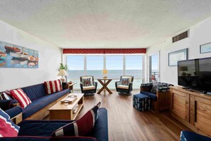 A living room with a sofa, chairs, a coffee table, a TV, and a view of the sea. - Updated OCEANFRONT condo with pool on the Boardwalk!!! (Virginia Beach)