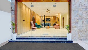 Un hall d’hôtel moderne avec une façade en pierre, une entrée en verre et un espace salon doté de différents types de fauteuils.
