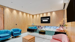 Un espace d’accueil moderne avec un mur revêtu de panneaux en bois, un panneau indicateur noir, des sièges bleus et roses, et une cloison en verre.