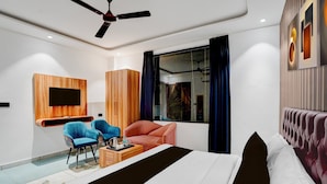 Une chambre d’hôtel moderne équipée d’un lit, de deux fauteuils, d’une télévision, d’un ventilateur de plafond et d’une fenêtre avec des rideaux.