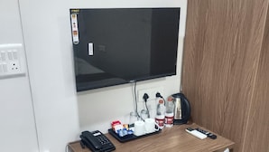 Une chambre d’hôtel avec un bureau en bois, une chaise, un téléviseur fixé au mur, une poubelle et une prise électrique.