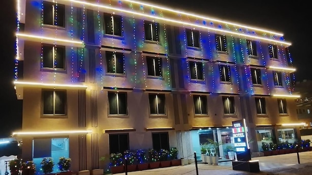 Un hôtel à plusieurs étages, avec une rangée de fenêtres, une enseigne indiquant qu’il s’agit d’un hôtel, et des plantes en pot devant l’entrée.