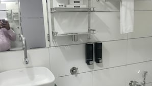 Une salle de bain avec un lavabo blanc, un miroir, un porte-serviettes et une douche.