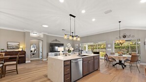 A spacious kitchen with a central island, a dining area with a table and chairs, and a large window providing a view of the outdoors. - Charming 3-bedroom house in the heart The Villages (The Villages)