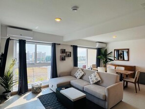 Uma sala de estar moderna com sofá, mesa de jantar e vista para o horizonte urbano através de grandes janelas.