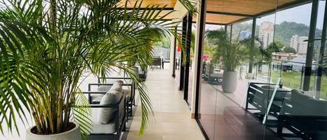 Een gang met zitplaatsen, een grote potplant en uitzicht door glazen deuren.
