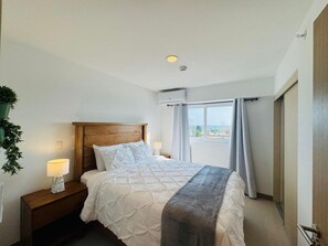 Quarto de hotel com cama, mesa de cabeceira, abajur e vista para o exterior.