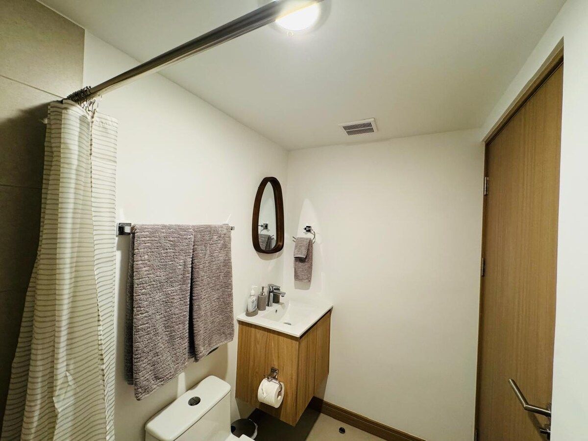 A small bathroom with a toilet, sink, and mirror. There is a towel rack with two towels and a shower curtain.