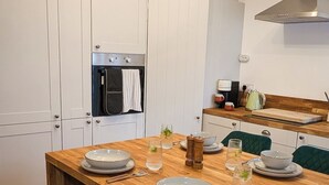Eine moderne Küche mit weißen Schränken, einem Holzespeisetisch, türkisfarbenen Stühlen und einer Pendelleuchte.