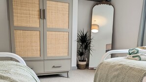 Ein Schlafzimmer mit zwei Betten, einem Kleiderschrank, einem Spiegel, einer Topfpflanze und einem Nachttisch.