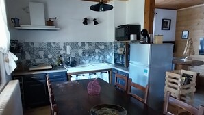 Een houten plafond, een keuken met een magnetron, een koelkast, een eettafel met stoelen en een betegelde spatwand.