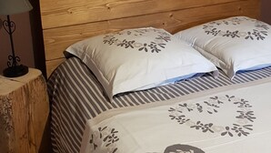 Een slaapkamer met een houten hoofdbord, een bed met beddengoed met bloemenprint, een nachtkastje met een lamp en een hartdecoratie aan de muur.