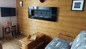 Een gezellige kamer met een houten plafond, een opgehangen hertenkop, een flatscreen televisie, een bank met gestreepte kussens en een klein houten tafeltje.