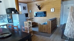 Een houten interieur met een eethoek, een bank, een opgehangen hertenkop en een televisie.