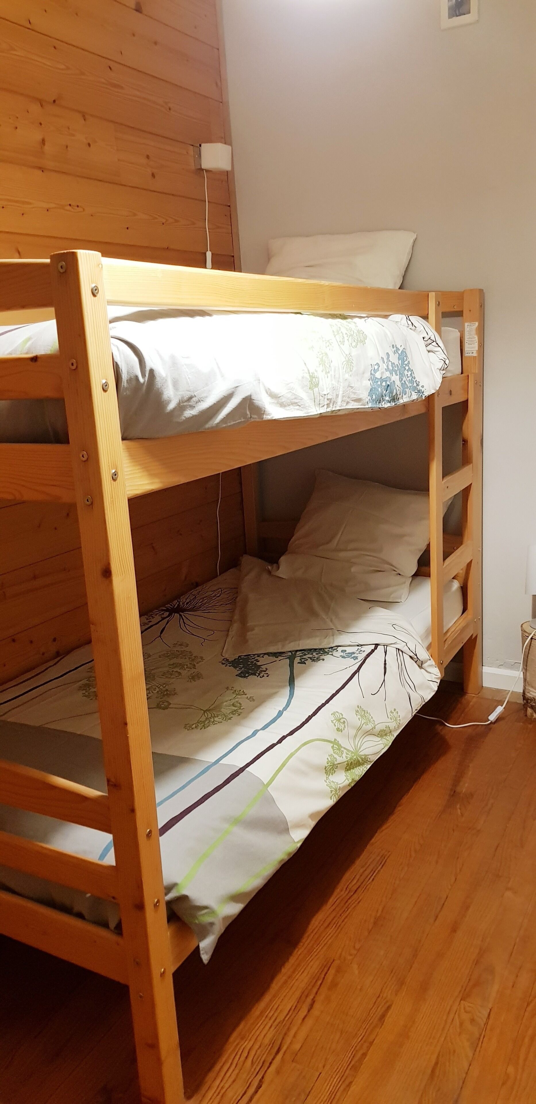 A bunk bed with a wooden frame, a floral bedspread, and a white pillow.