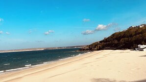 Ein Strand mit blauem Himmel, sandigem Ufer und einigen Gebäuden in der Ferne.