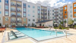 A multi-story hotel with a swimming pool, outdoor seating, and balconies. - Riviere Apartments King Bed Suite & Pool & Gym & Pet Friendly & Near Epic Universe (Orlando)