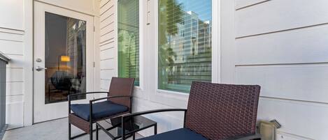 Un patio con dos sillas de mimbre, una mesa, una puerta y una ventana con persianas.