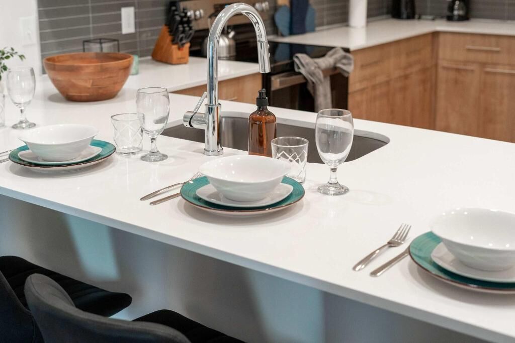 A modern kitchen with a white countertop, stainless steel faucet, and a wooden bowl.